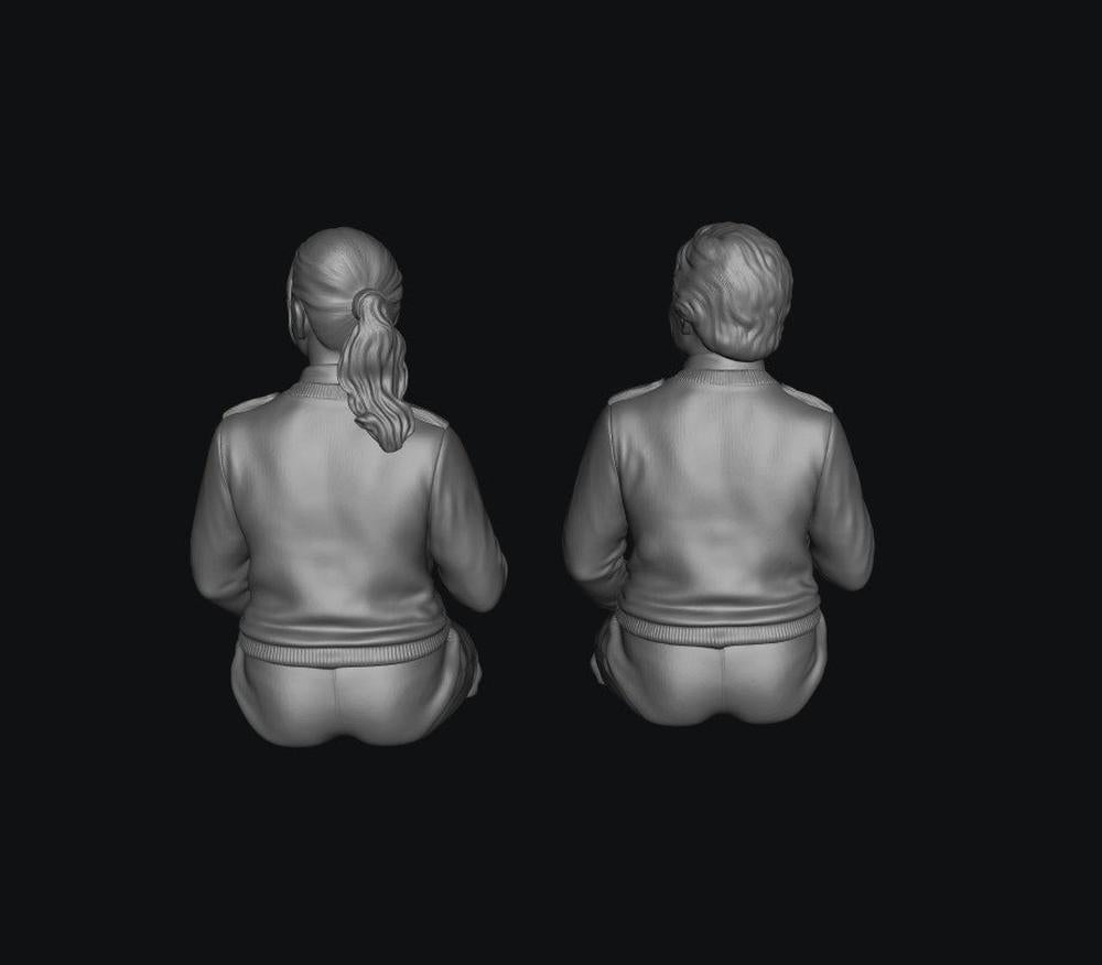 Two unpainted grey 3D-printed resin scale model figures of female bus drivers seen from behind.