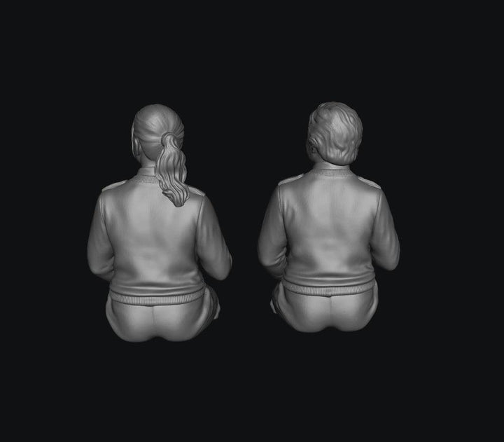 Two unpainted grey 3D-printed resin scale model figures of female bus drivers seen from behind.