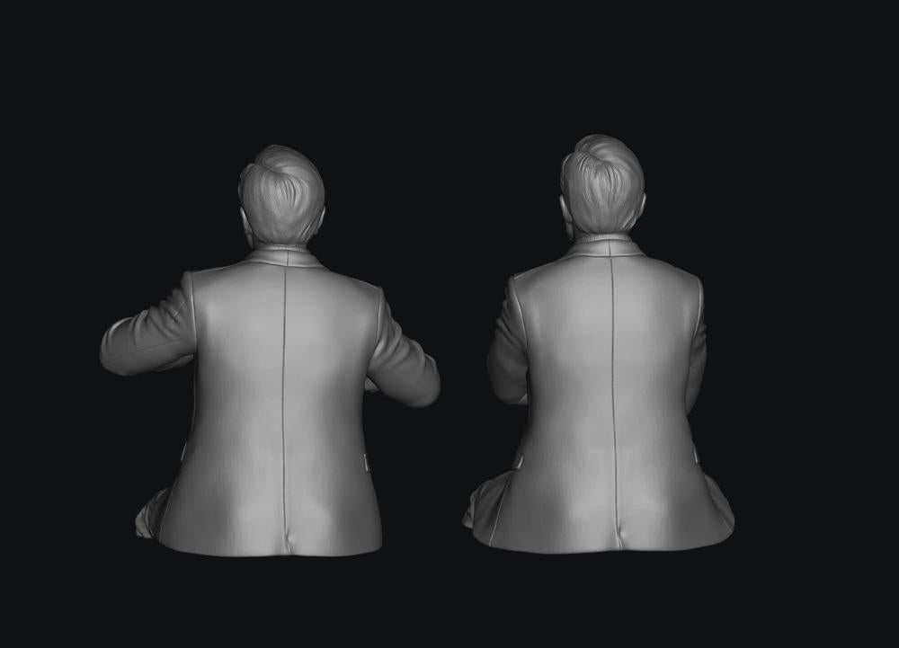 Two unpainted grey 3D-rendered figures of seated train crew members in suit jackets, viewed from behind.