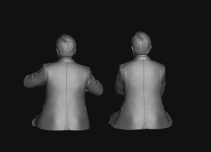 Two unpainted grey 3D-rendered figures of seated train crew members in suit jackets, viewed from behind.