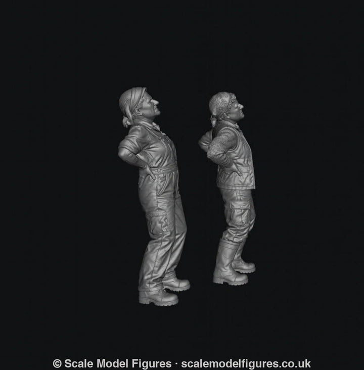 Two unpainted grey resin 3D-printed miniature figures of female farmers standing with hands on their aching backs.